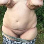 Halfway naked. Pausing with arms out of shirt sleeves, and trousers lowered. For something to do with her hands she decides to grab her big tits and spread them apart. All lovely !
