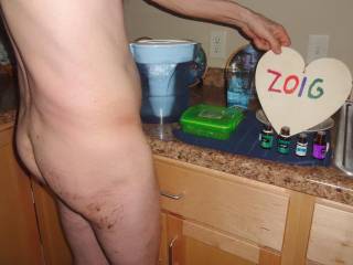 A very partial butt and body view as I stand near a counter with a zeropoint water pitcher, a glass & essential oils that I will take internally. My butt is messy with purple lube residue as I am on vacation, so, i can toy play. Sony WX150 camera is used.
