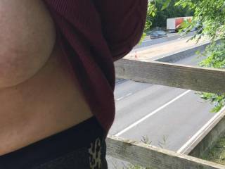 Kindly standing on a motorway bridge so he can look at the trucks and her tits