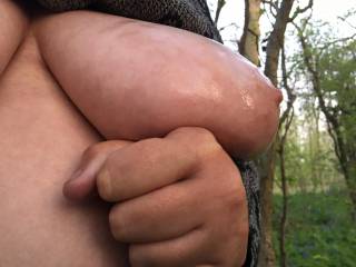 Left tit only, a side view, baby oil added, supporting hand below, woodland in background