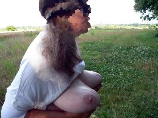 Wearing sunglasses standing on a hilltop, showing her oiled big tits to a friend