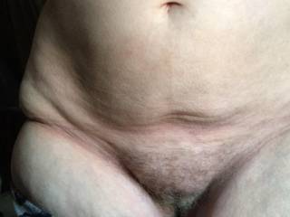 A hairy lady stands waiting for the guest crouching behind her to finish pulling down her underwear - having first kissed her big tits while getting her topless